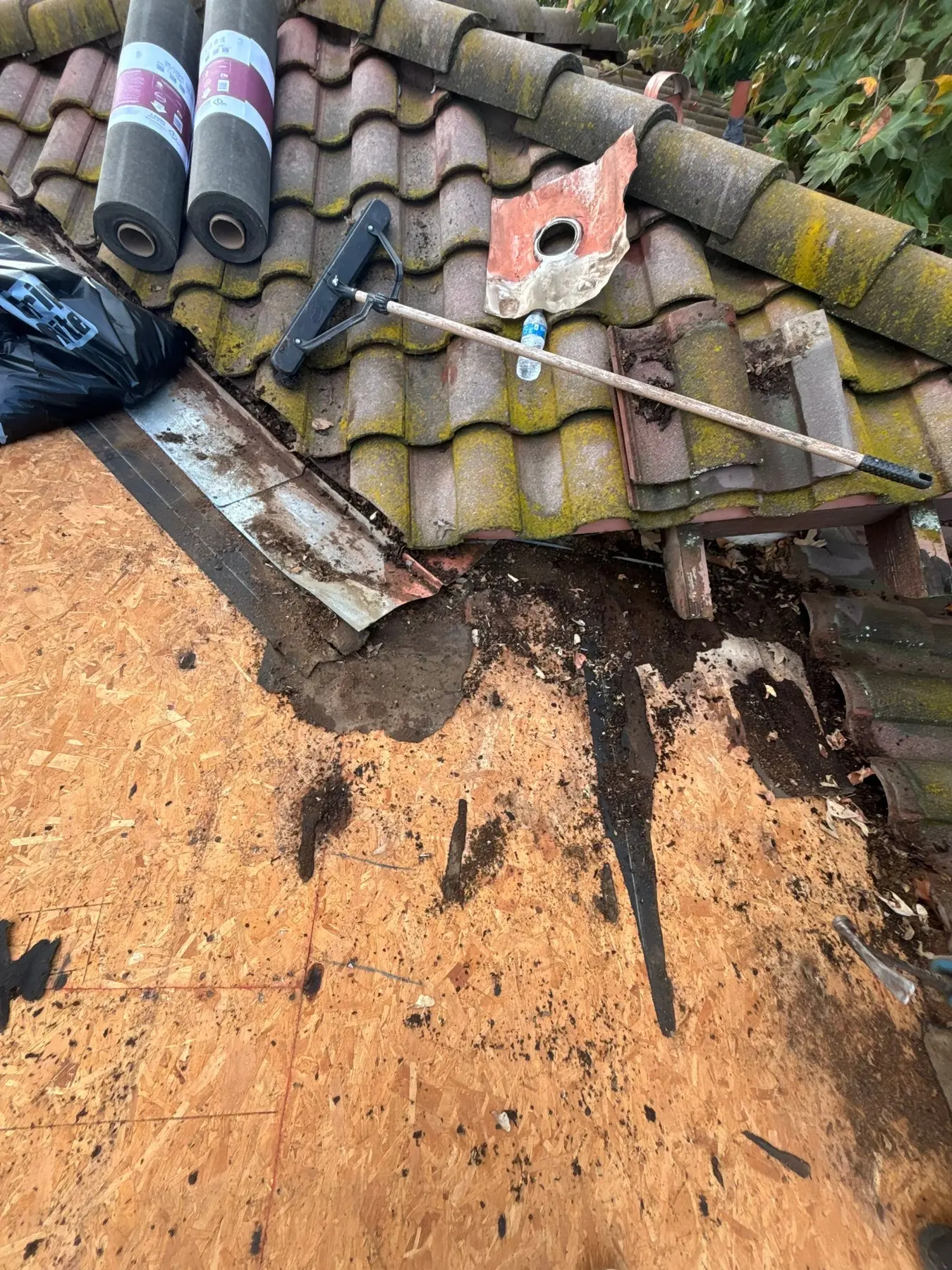 Debris and deteriorated flashing exposed at a tile roof drainage channel