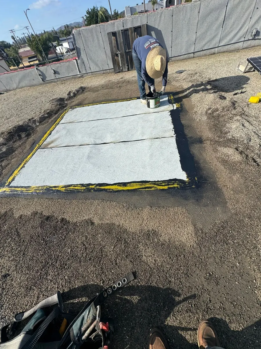 Roofer reinforcing the perimeter of a built-up roof repair with fiberglass fabric and roofing cement