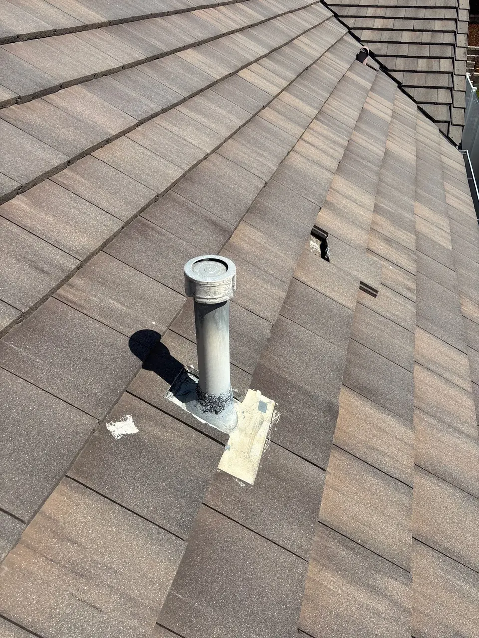 Exposed underlayment beside a concrete roof tile and vent pipe