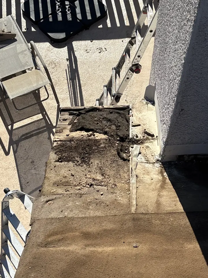 Debris and deteriorated roof material collected behind a tile roof chimney