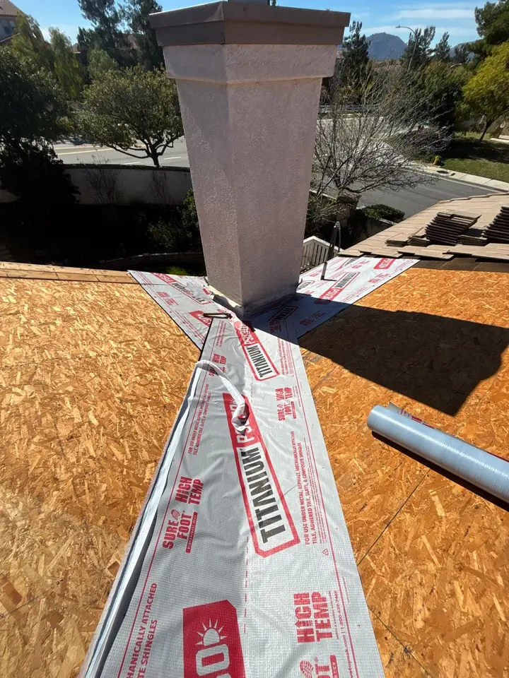 Tile and underlayment removed around a chimney revealing accumulated debris and damage