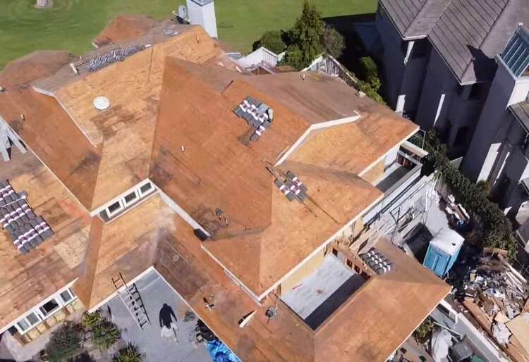 Tile roof replacement in progress with the roof deck exposed and new tile staged