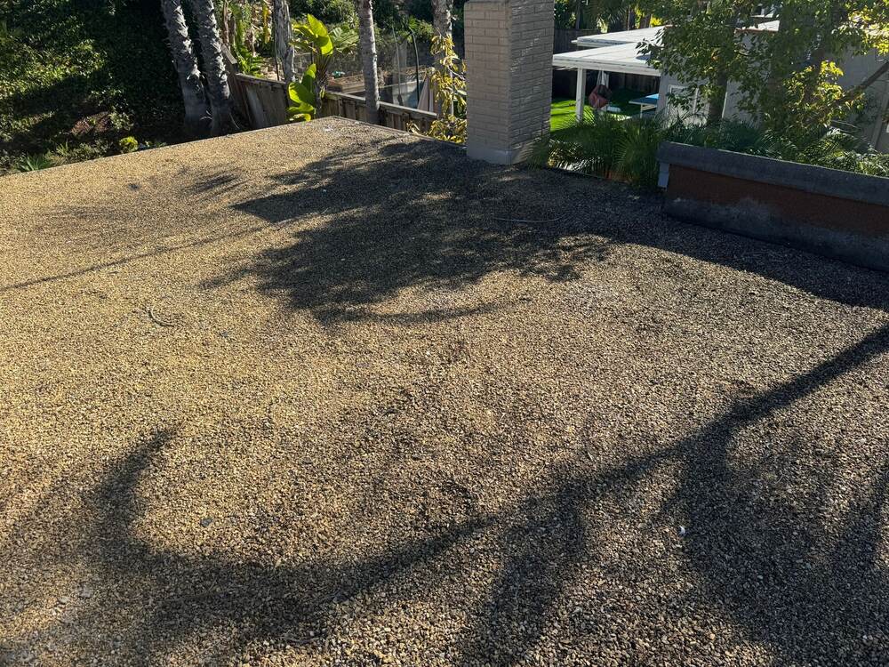 Existing tar-and-gravel low-slope roof around a chimney before roofing work
